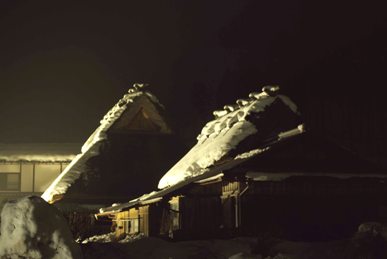 灯りに照らされた雪のかやぶき屋根の家