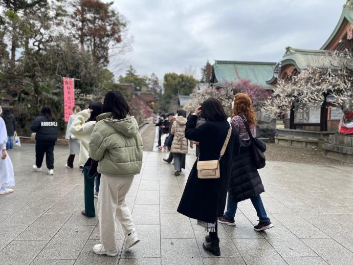 ウォーキングイベントにて、学生と外国人女性が梅の花を見ている様子